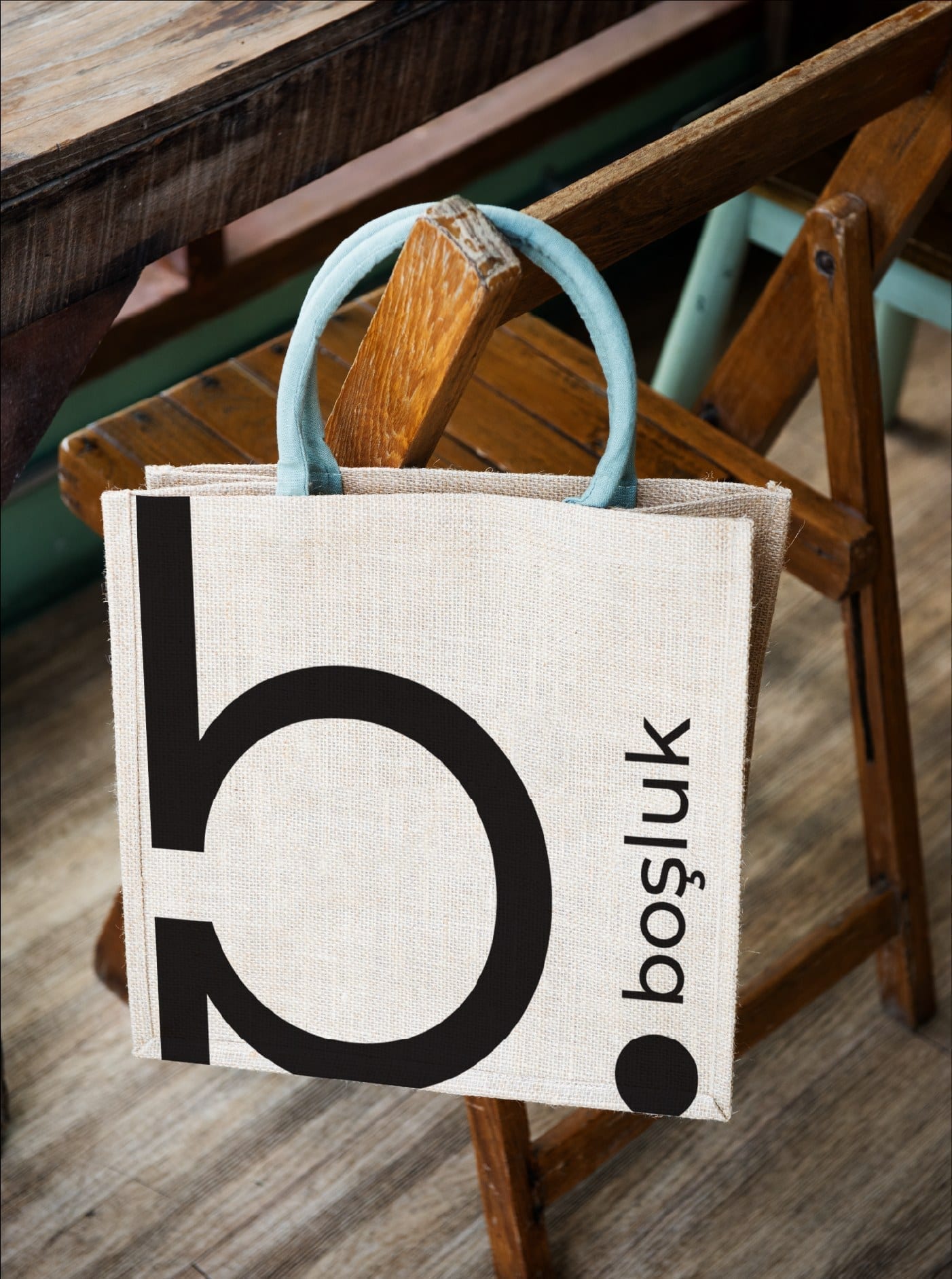 Boşluk tote bag hanging from a wooden chair, large logo centered on the cream canvas.