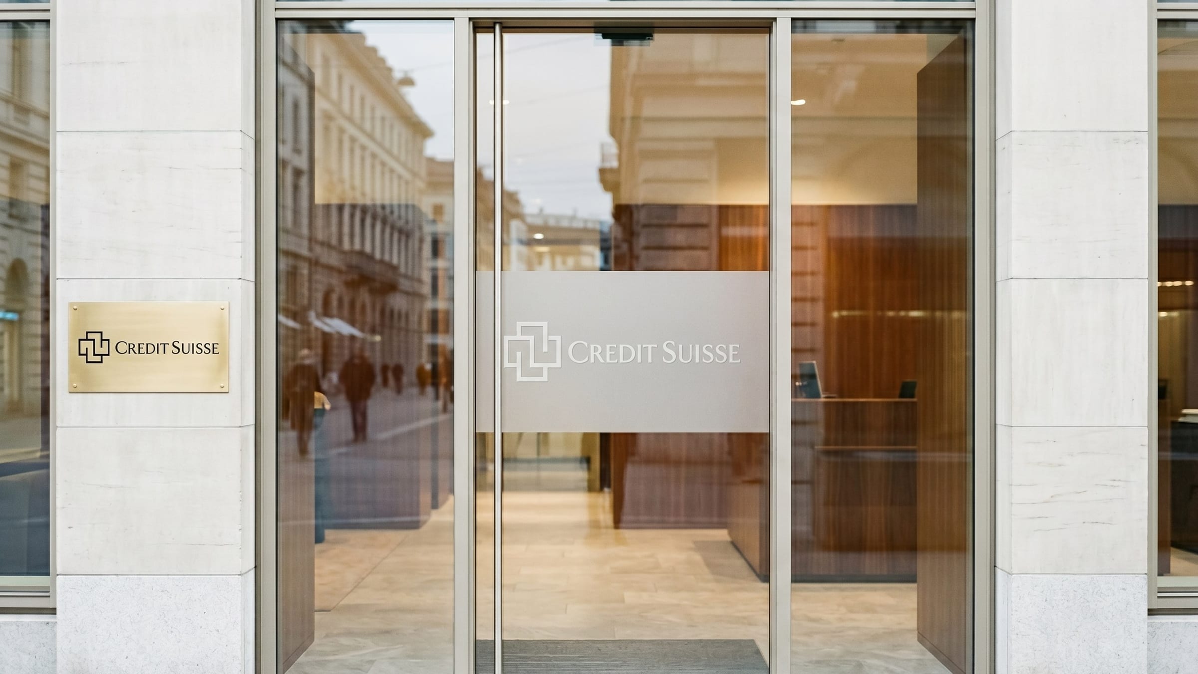 Branch entrance glass door with frosted vinyl logo panel at eye level, showing the mark at human scale.