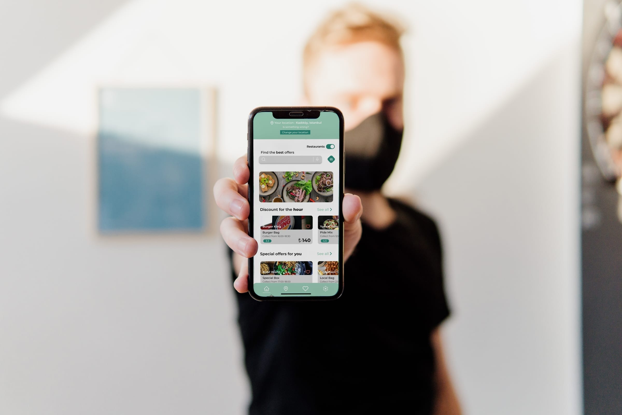 Person holding a phone showing the GreenPlates+ home screen with offer listings.