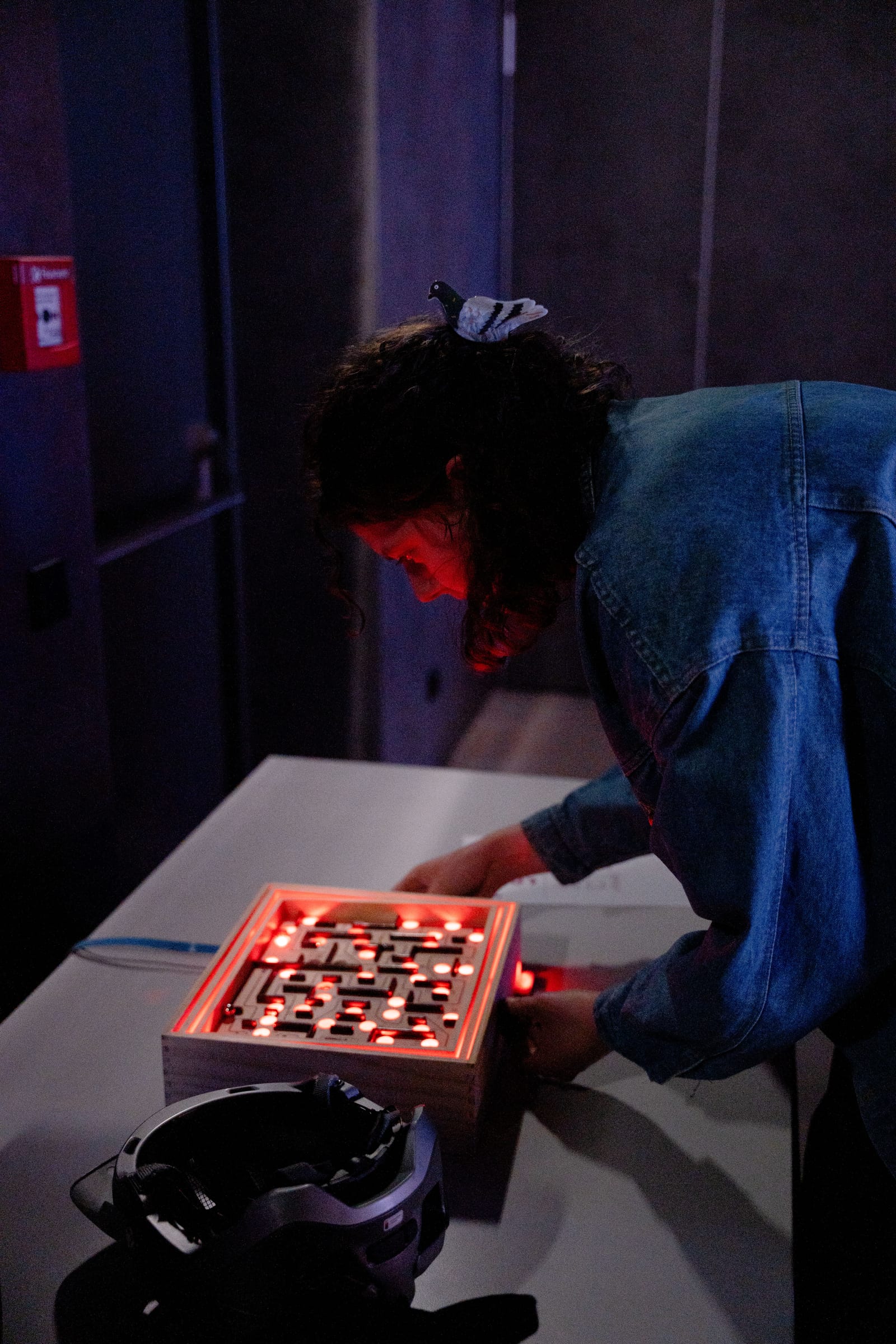 A second player leans over the red-lit labyrinth board, guiding the ball, a VR headset resting on the table in the foreground.