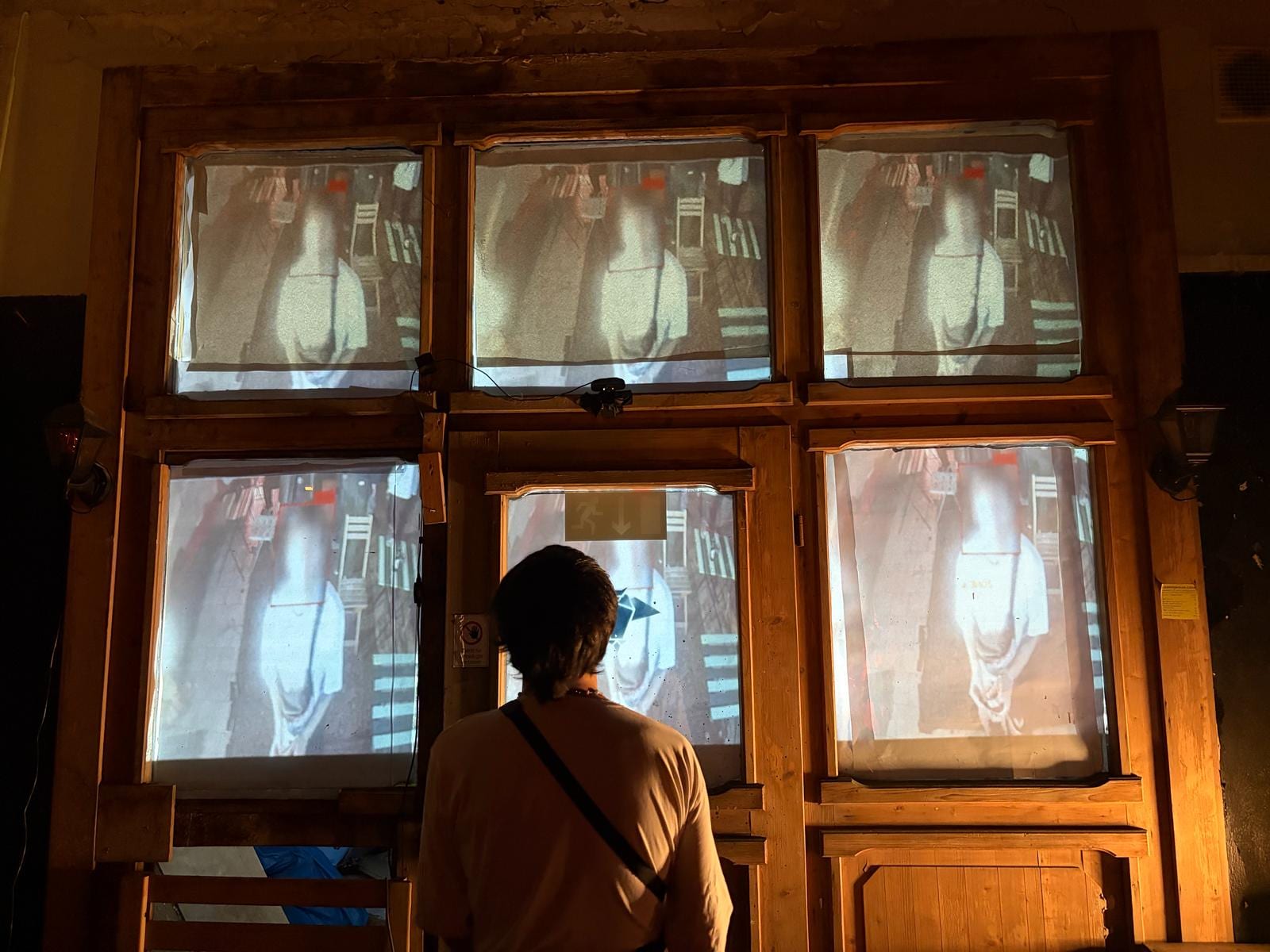 A visitor stands in front of the installation as the window panes display live camera captures of people with red face-detection bounding boxes overlaid on their heads.