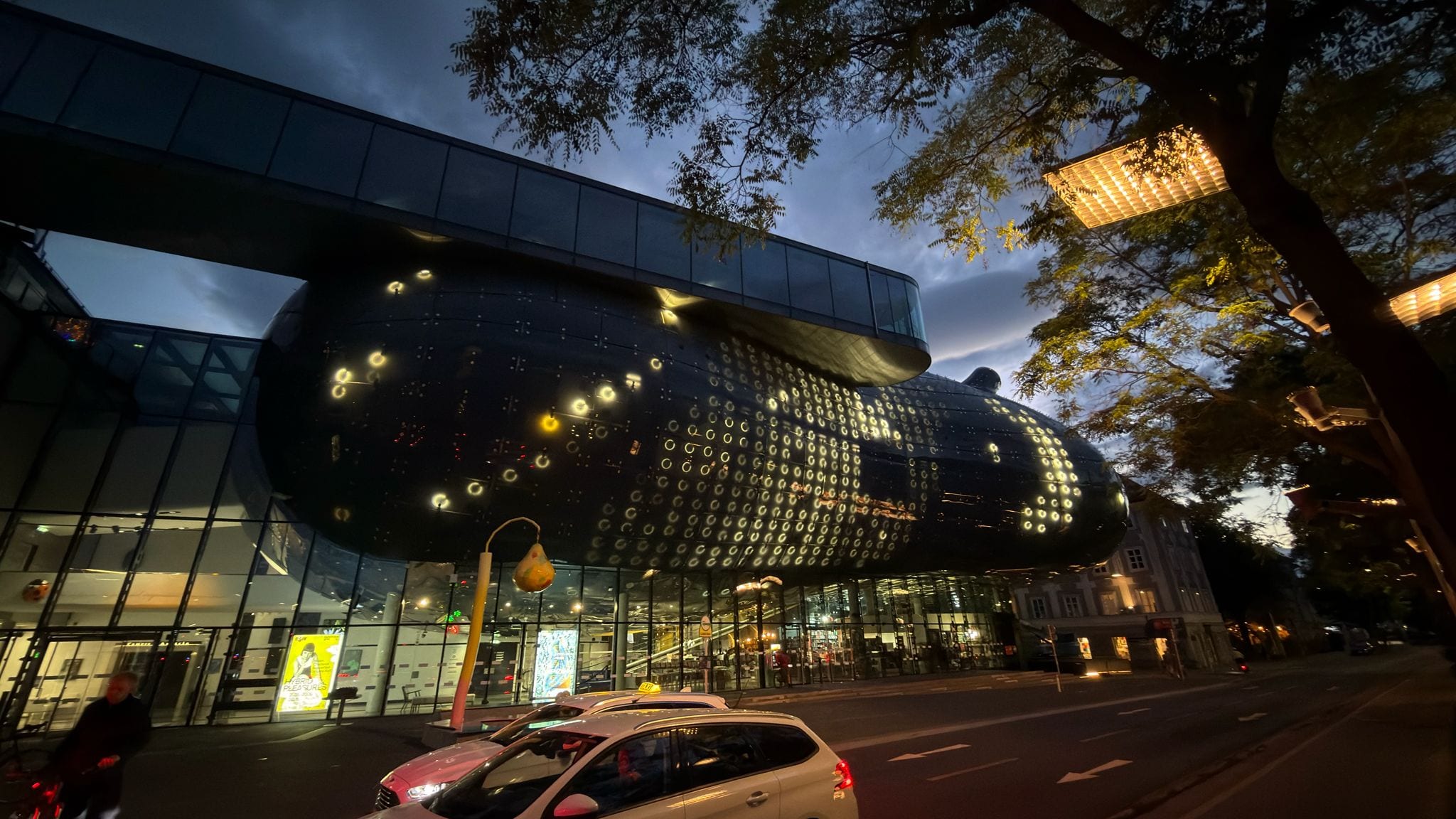 The Kunsthaus Graz "Friendly Alien" building at night, its BIX facade of illuminated rings glowing against the sky.